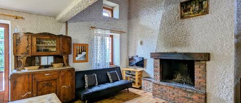 A rustic room with a stone wall, a fireplace, a wooden cabinet, a black sofa, and a television.