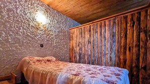 Una cama individual en una habitación con pared de piedra texturizada y paneles de madera.