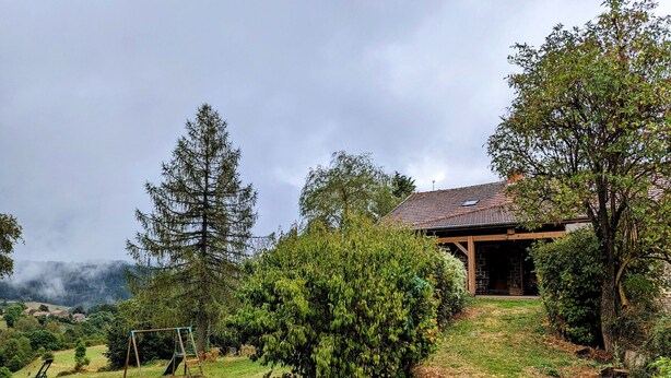 Una casa rústica con base de piedra y techo de tejas, rodeada de abundante vegetación y árboles.