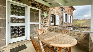 Un bâtiment en pierre doté d’un patio couvert, d’une table ronde en bois et de quatre chaises en bois.