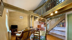 Un salon chaleureux avec un canapé en cuir, une table à manger en bois avec des chaises, un téléviseur et un escalier menant à une cuisine.