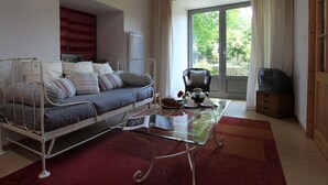 A bedroom with a metal bed frame, a glass coffee table, a red carpet, a chair, and a television. - Restored 19th-Century Farmhouse with Garden, Near Trails & Attractions (Saint-Julien-Chapteuil)
