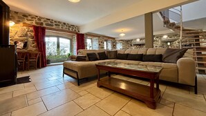 A spacious living room with a stone wall, a large beige sofa, a wooden coffee table, and a staircase leading to an upper level. - Restored 19th-Century Farmhouse with Garden, Near Trails & Attractions (Saint-Julien-Chapteuil)