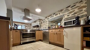 A kitchen with a stone wall, wooden cabinets, a stainless steel oven, and a microwave. - Restored 19th-Century Farmhouse with Garden, Near Trails & Attractions (Saint-Julien-Chapteuil)