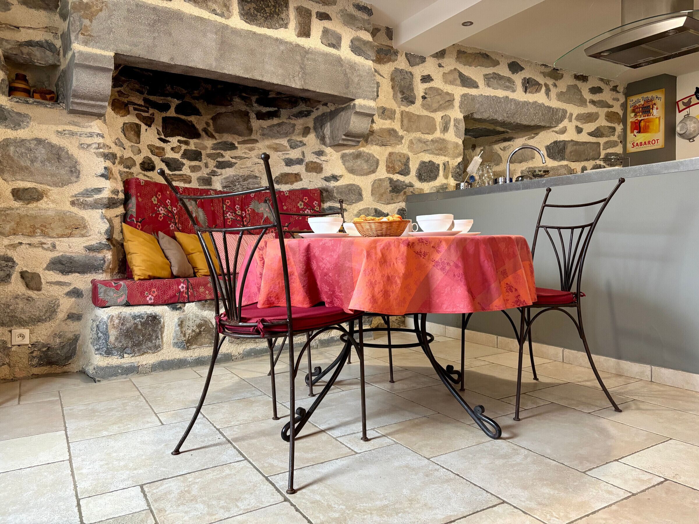 A stone-walled dining area with a table set for two, featuring a red tablecloth and metal chairs.