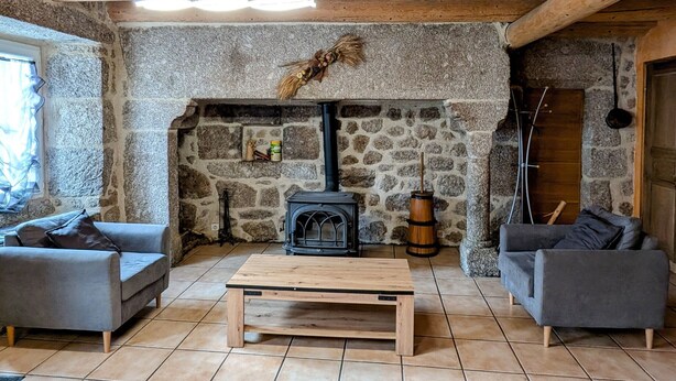 Un salon chaleureux avec une cheminée en pierre, des poutres en bois et deux canapés gris.