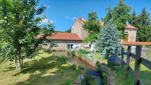 Un bâtiment en pierre avec un toit rouge, un petit ruisseau et un jardin clos.