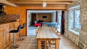 Un coin repas en bois avec une longue table et des chaises, une cuisine avec des meubles en bois et un mur en pierre.