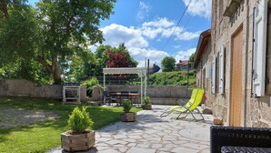 Un espace patio doté d’un sol en pierre, de mobilier d’extérieur, d’un barbecue et offrant une vue sur un bâtiment en pierre.