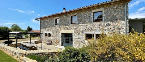 A stone house with a patio, a covered seating area, and a garden with flowering plants.