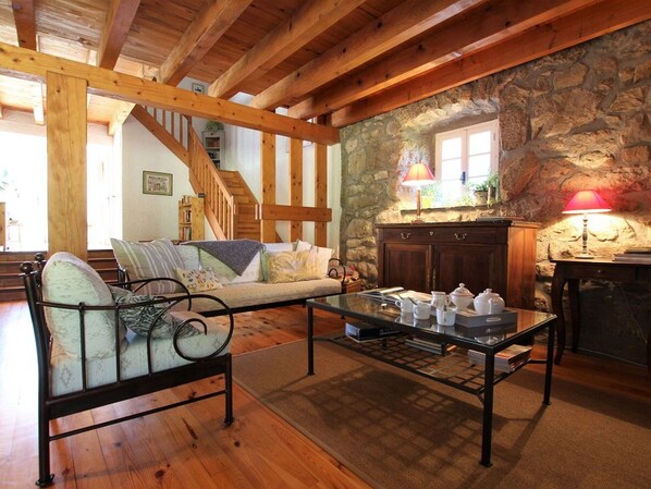 Uma sala de estar aconchegante com parede de pedra, vigas de madeira, sofá, mesa de centro e lareira.