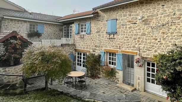 Un bâtiment en pierre doté d’une cour intérieure, avec une table et des chaises, une clôture blanche et une enseigne sur laquelle on peut lire « La Tranquille ».