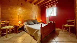 Une chambre dans une cabane en bois, comprenant un lit, deux tables de chevet, deux chaises, une fenêtre avec des rideaux et un plafond en bois.