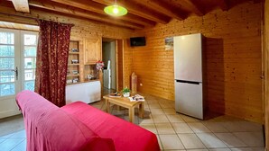 L’intérieur d’un chalet accueillant, avec un plafond en bois, un canapé rouge, une table à manger agrémentée d’un vase et un réfrigérateur.
