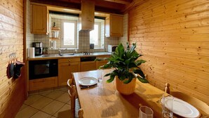 Une cuisine rustique aménagée dans une cabane en bois, avec une table à manger, des chaises, une machine à café et une plante en pot.