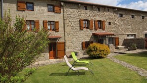 A stone building with multiple windows and doors, a small garden with a lawn and a bush, and two outdoor chairs.