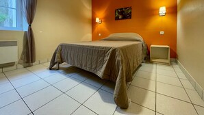 A hotel room with a bed, a nightstand, a wall-mounted lamp, and a window with curtains.