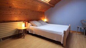 A cozy attic bedroom with a sloped ceiling, a skylight, a bed, a small table, and a chair.