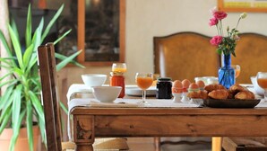 A wooden dining table with a white tablecloth, a vase with pink flowers, a bowl, a glass of orange juice, a bottle of ketchup, eggs, and croissants.