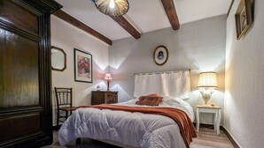 A bedroom with a large bed, a wooden chair, a small table with a lamp, and a picture on the wall. - Charming House with Terrace, Garage, and Activities near Allier Gorges (Mazeyrat-d'Allier)