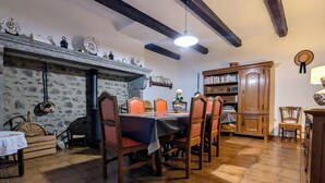 A dining area with a stone wall, wooden beams, a tiled floor, and a bookshelf. - Charming House with Terrace, Garage, and Activities near Allier Gorges (Mazeyrat-d'Allier)