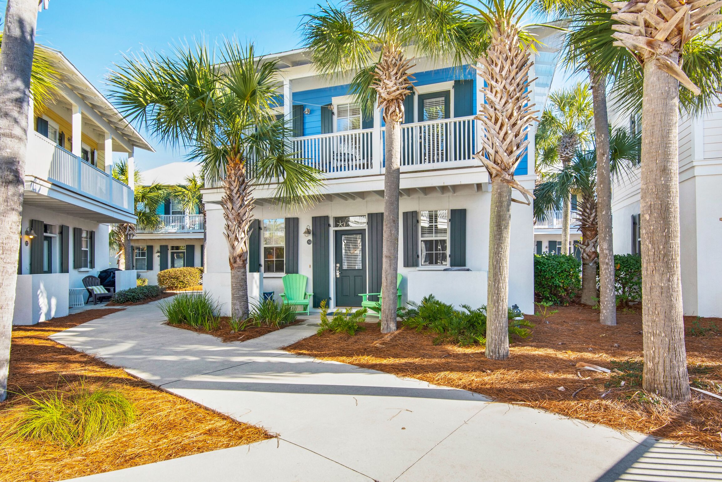 A coastal residential area with two-story houses, a paved walkway, and palm trees.