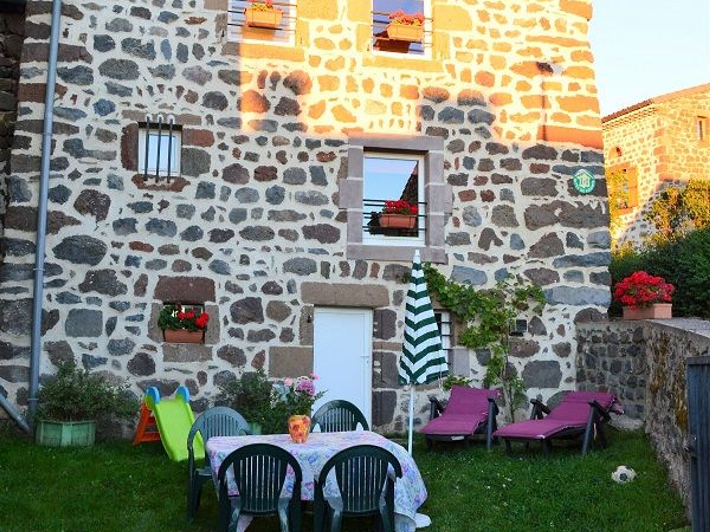 Un edificio de piedra con un pequeño balcón, una puerta y una mesa con sillas afuera.