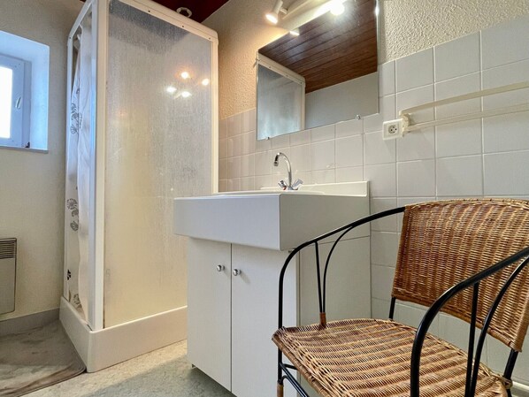 Une salle de bain avec une douche, un lavabo, un miroir et une chaise en osier.