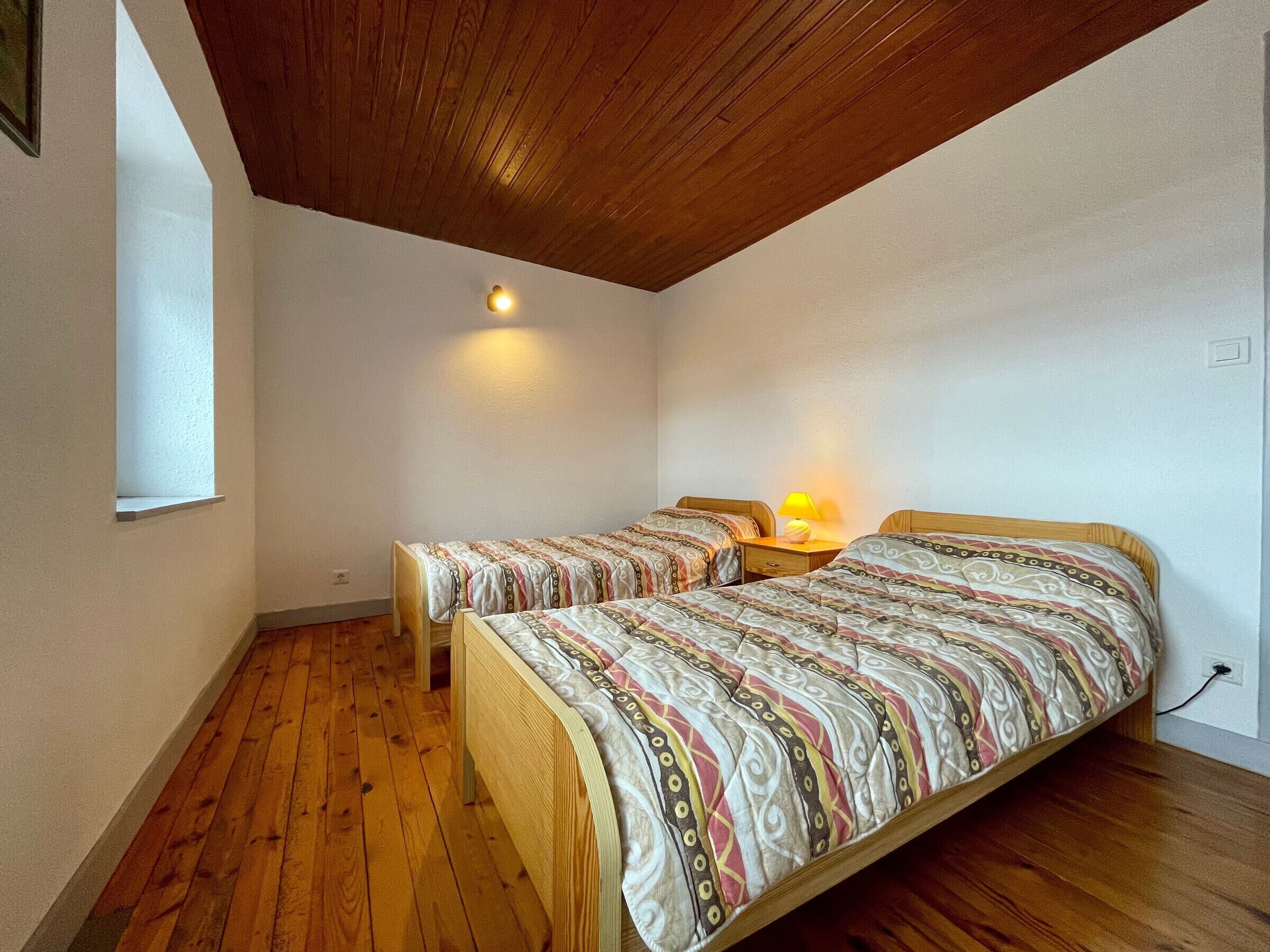 A small, cozy room with two wooden beds, a single window, and a wooden ceiling.