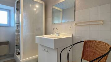 Een badkamer met een witte wastafel, spiegel en rieten stoel.