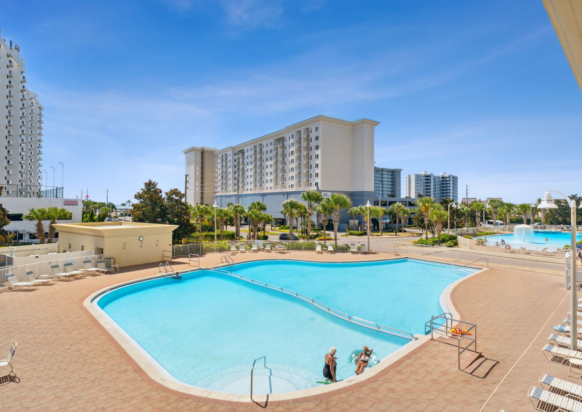 A large outdoor swimming pool with a clear blue water, surrounded by lounge chairs and palm trees.