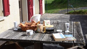 A wooden picnic table with a basket of bread, a coffee maker, a mug, a book, and a bag of Mate tea.