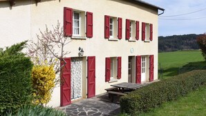 A two-story building with red shutters, a stone-paved entrance, and a small outdoor table.