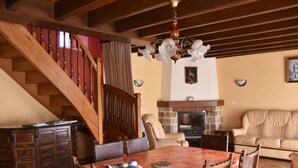 A dining area with a wooden table and chairs, a fireplace, a sofa, and a staircase.