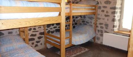 A room with bunk beds, a stone wall, a window with a view, and a radiator.