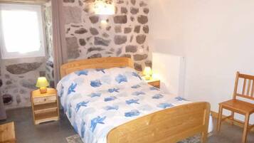 Une chambre avec un mur en pierre, un lit en bois, deux lampes de chevet, une chaise en bois et une fenêtre avec des rideaux.