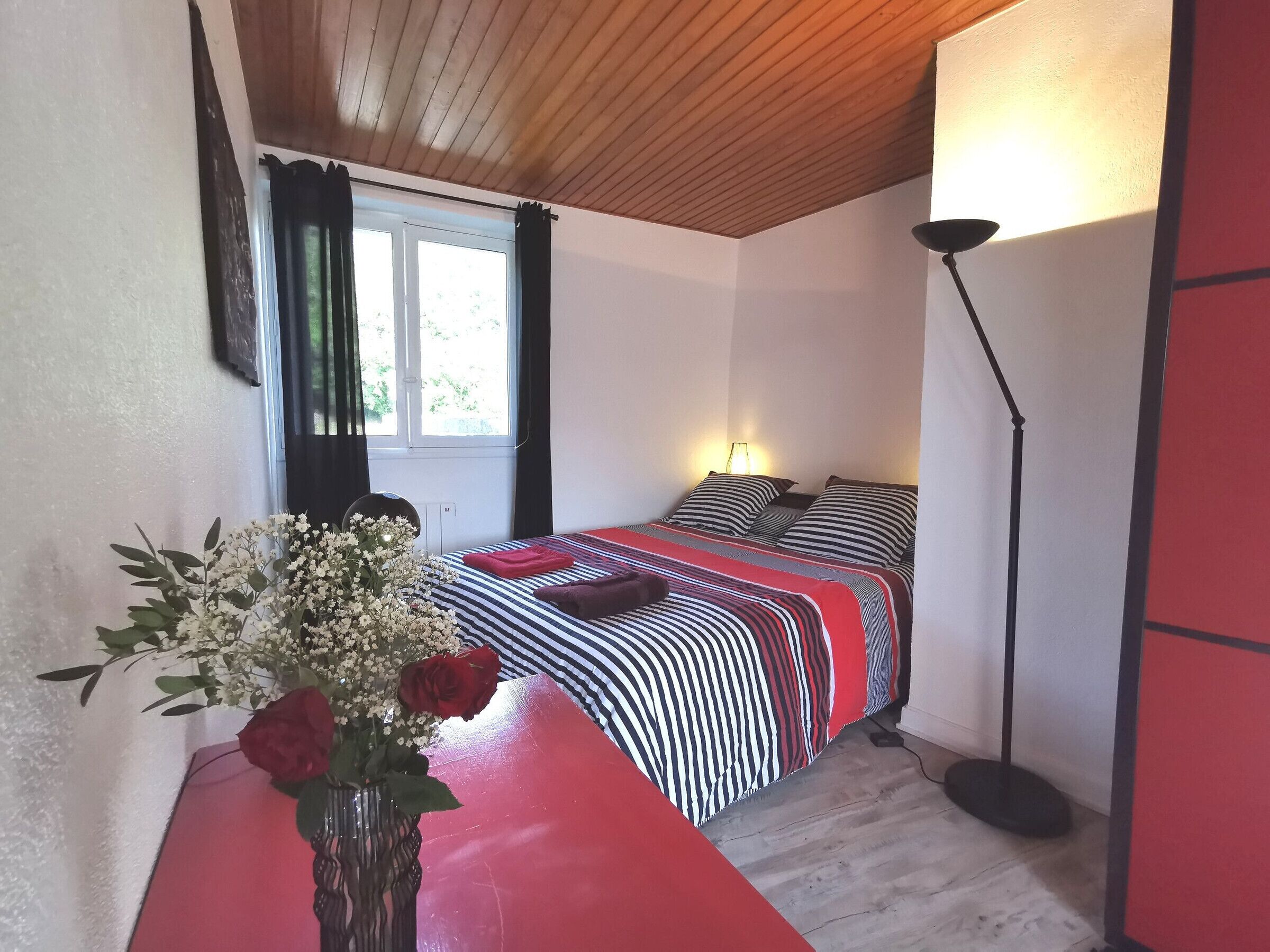 A bedroom with a bed, a bedside lamp, a vase with flowers, and a window with curtains.