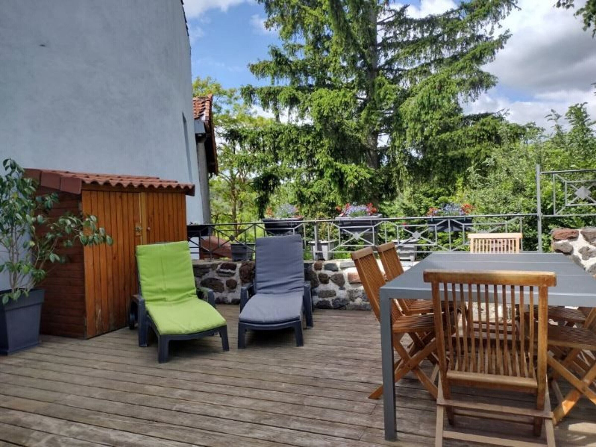 Eine Terrasse im Freien mit Tisch und Stühlen, umgeben von viel Grün und einer Steinmauer.