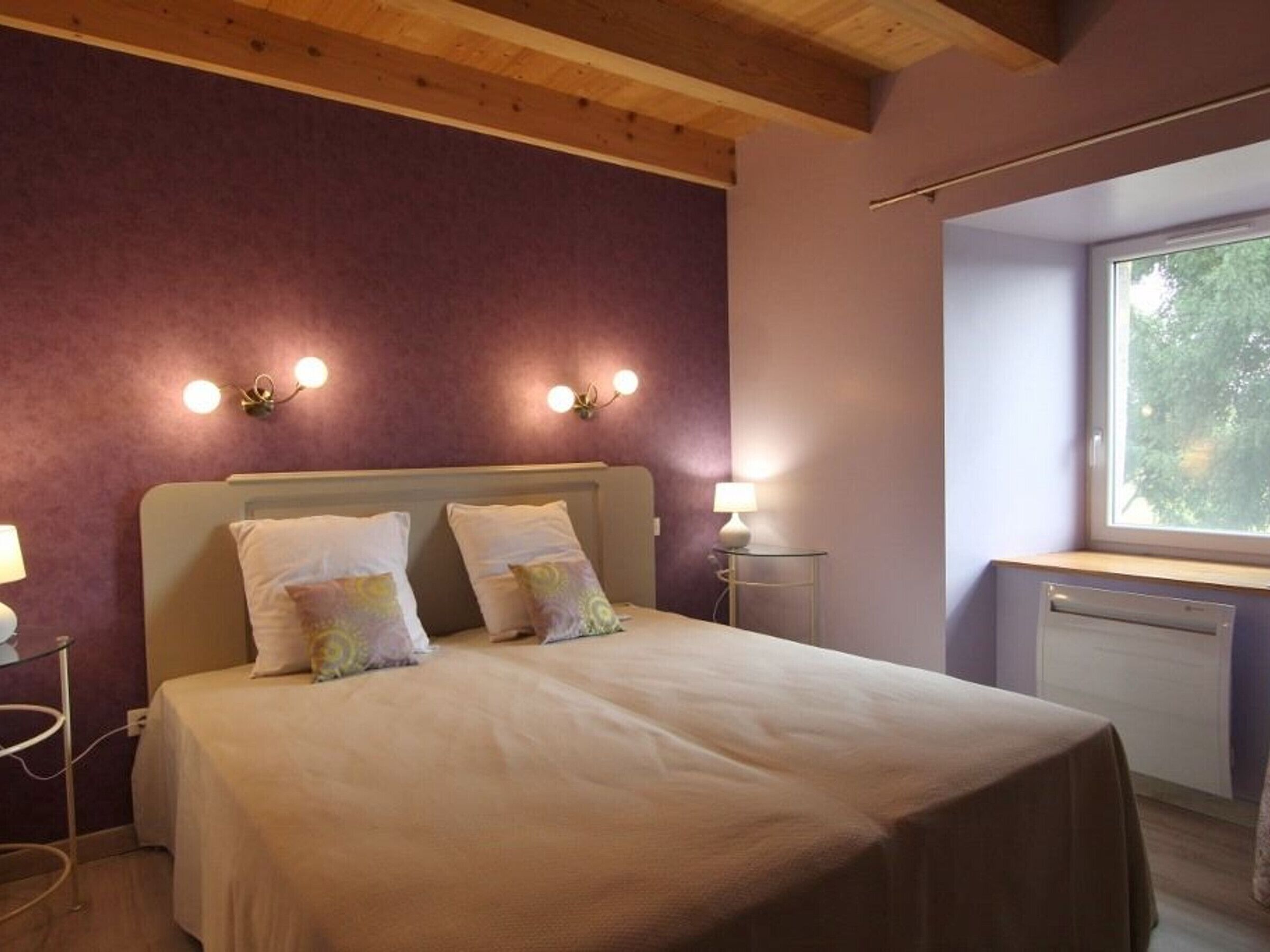 A bedroom with a bed, two bedside lamps, a window with a view, and a wall-mounted light fixture.
