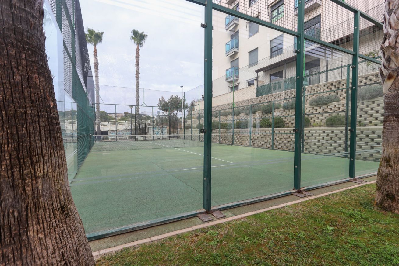 Ein Tennisplatz im Freien, umgeben von einem grünen Zaun, mit einem Gebäude im Hintergrund.