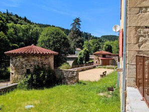 Un bĂątiment en pierre surmontĂ© dâun toit de tuiles rouges, un pont de pierre et une vĂ©gĂ©tation luxuriante.