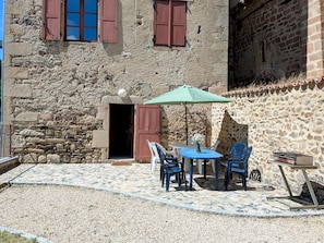 Un bĂątiment en pierre dotĂ© dâun patio comprenant une table et des chaises, un barbecue et une porte donnant accĂšs Ă un espace intĂ©rieur.