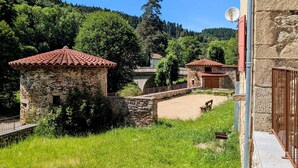 Un edificio de piedra con tejado de tejas rojas, un puente de piedra y abundante vegetación.