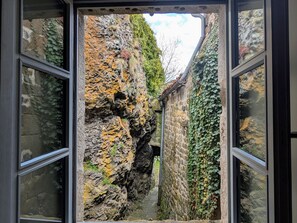 Une étroite ruelle pavée, bordée de murs couverts de lierre et d’un bâtiment en pierre au style rustique.