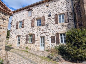 Un bâtiment en pierre doté de nombreuses fenêtres, un chemin pavé et un petit espace aménagé en jardin.