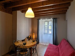 Un coin repas avec une table en bois, des chaises, un luminaire suspendu, une fenêtre avec des rideaux et un canapé rouge.
