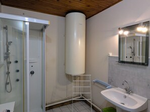 A bathroom with a glass shower enclosure, a white sink, a mirror with lights, and a white water heater.