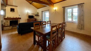 A spacious room with a wooden dining table, chairs, a sofa, a fireplace, and a window with curtains.