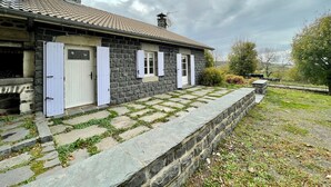 A stone house with a tiled roof, a stone pathway leading to the entrance, and a grassy area with trees.