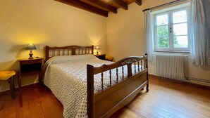 A bedroom with a wooden bed, two bedside tables with lamps, a window with curtains, and a radiator.